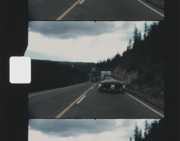 Vehicle drives on highway next to mountain forest
