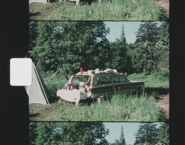 A tent and station wagon are set up in a forest clearing