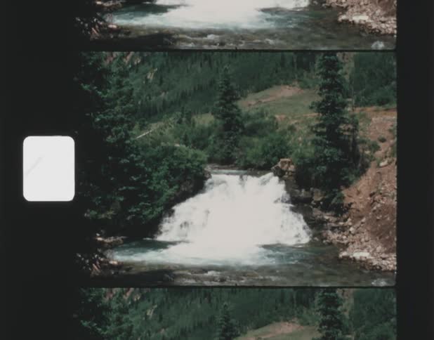 A river flows swiftly downhill in a mountainous area surrounded by trees
