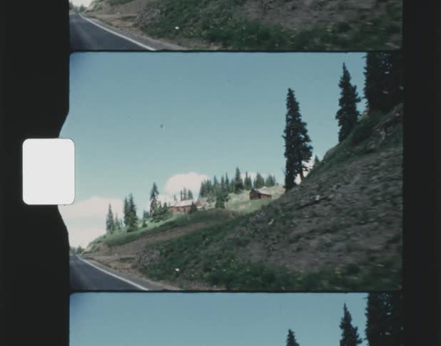 Highway passes by cabins on hills and conifers on mountains
