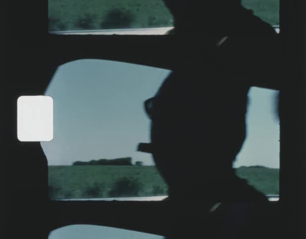 A man has a cigar in his mouth as he looks out the window of a traveling automobile