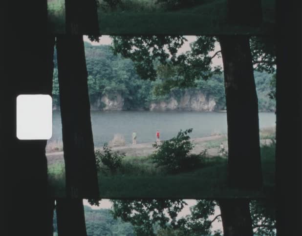 People on bank of lake seen from between trees in the forest