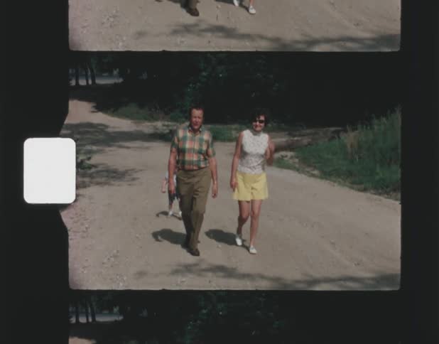 Father with plaid shirt and green pants and mother with sunglasses white top and yellow skirt walk uphill in front of their toddler son