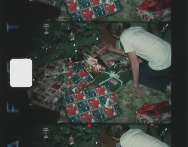A young boy excitedly reaches for presents underneath a christmas tree