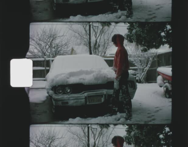 Young man runs hand through snow on vehicle before walking away from it