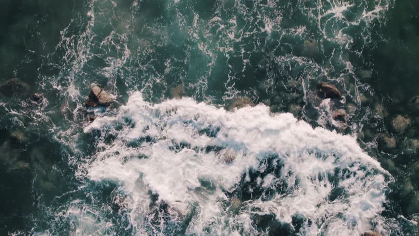 Waves foam while flowing over rock outcroppings in blue green ocean
