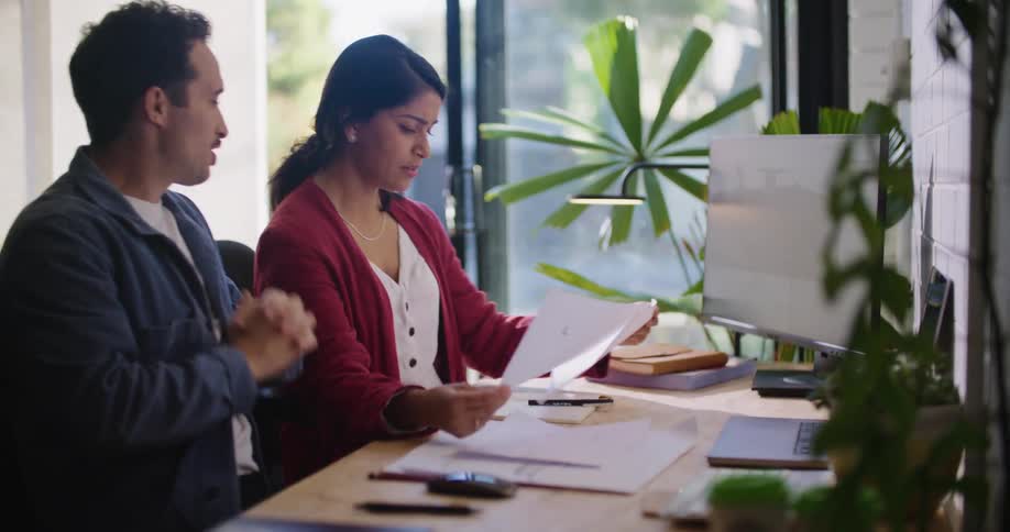A woman sits at a desk in an office when her male colleague arrives