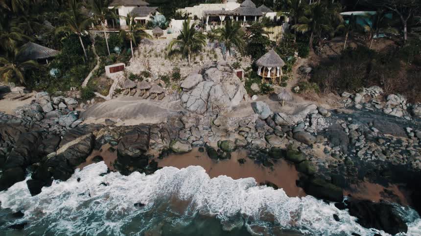 Aerial view of ocean waves breaking against the shore and holiday resort in the jungle