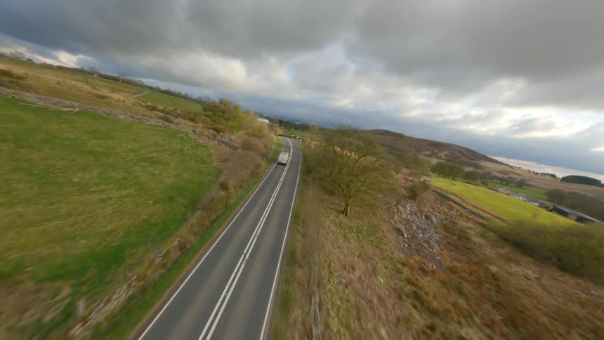 Vehicles drive past fields along a rural highway