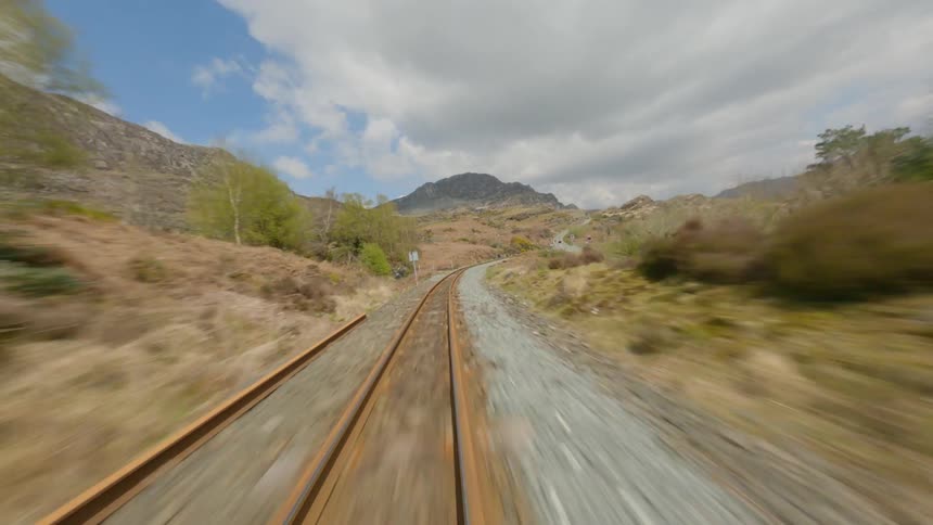 An aerial view of a rusty railroad track near hills and mountains