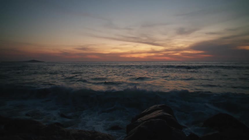 Landscape of ocean waves breaking against the rocky shore at sunset