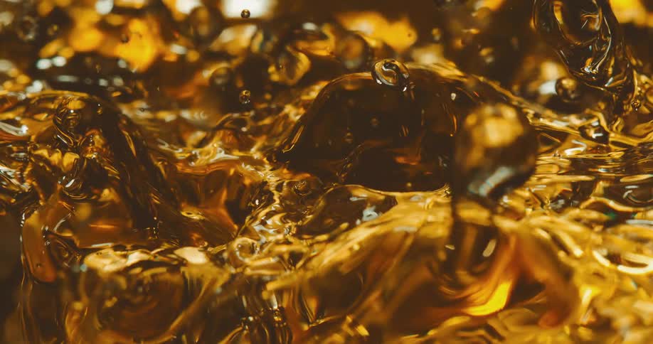 Drops splash as they fall into amber liquid creating ripples and waves