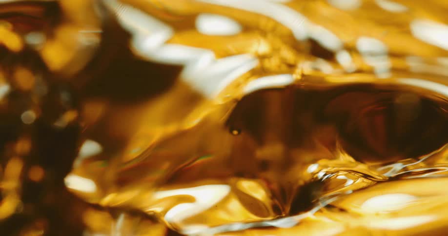 Drops fall onto amber liquid creating splashes and waves