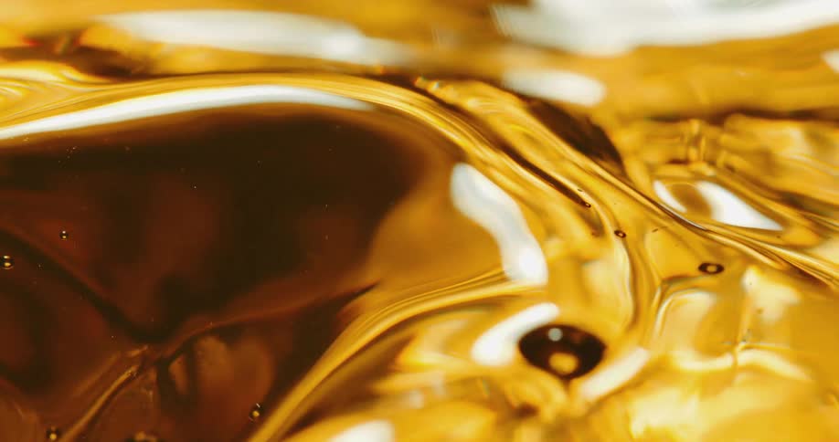 A droplet of liquid falls downward and splashes into an amber fluid