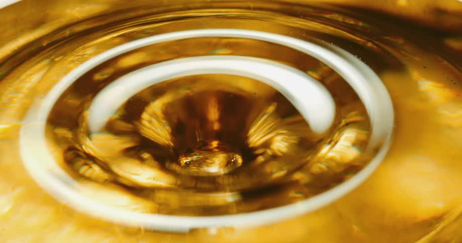 A clear sphere falls into a golden liquid and creates a rippling ring on the surface and splashes back up