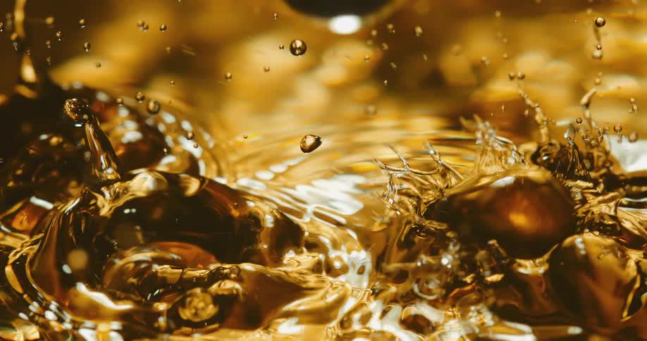 A gold clear liquid with droplets splashing the surface breaking the reflection