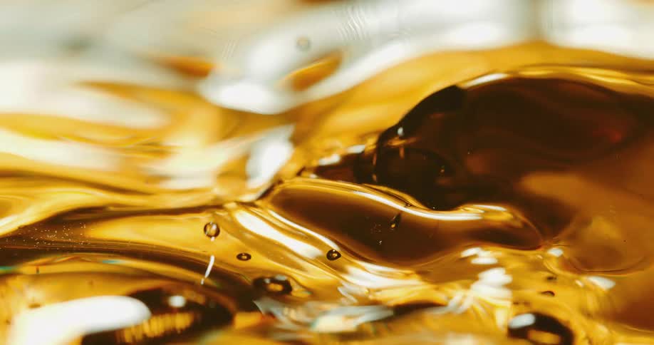 Droplets of an amber liquid fall and splash forming bubbles and ripples