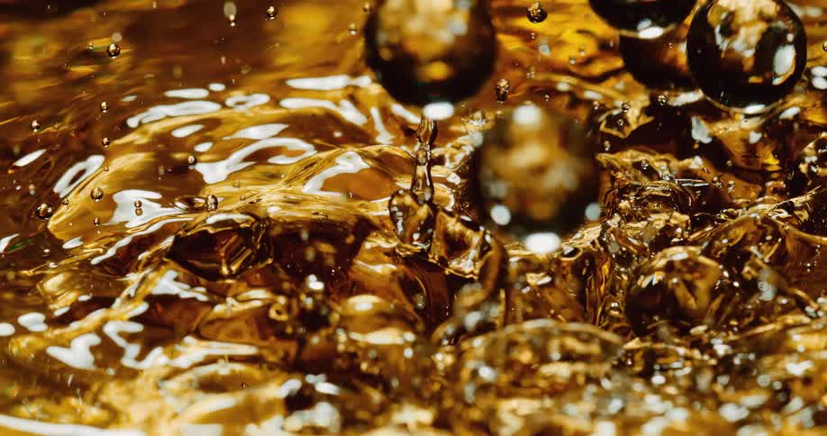 Clear orbs fall into a golden liquid and droplets fly into the air as they splash