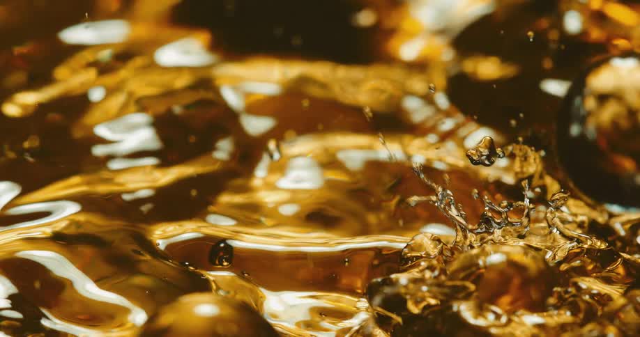 Clear spheres fall into a golden liquid and ripples move across the surface as tiny droplets fly into the air