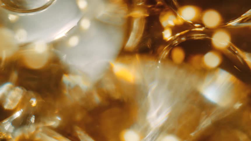 Yellow gold liquid with droplets and reflections cast on it