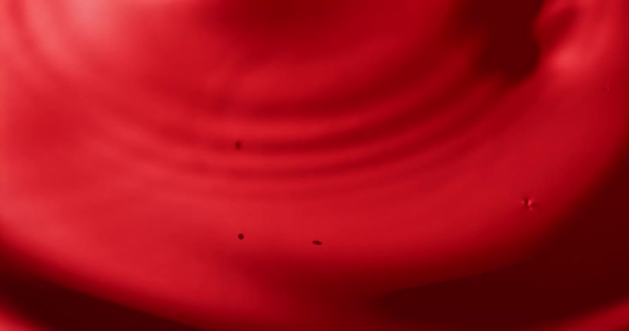 A close up of red paint being dropped into creating ripples on the smooth surface