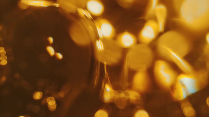 Amber syrup flows slowly reflecting blurry ring of lights