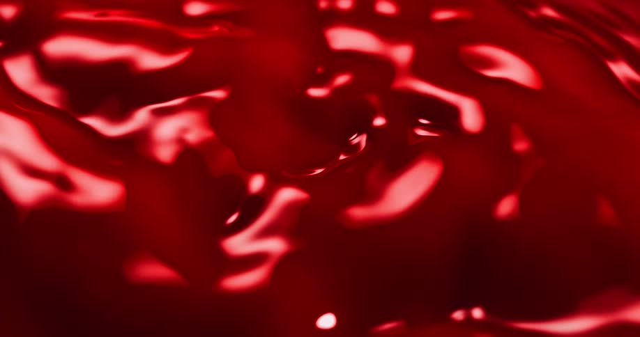 Light shines on an organic red liquid substance as it spreads and moves across the surface