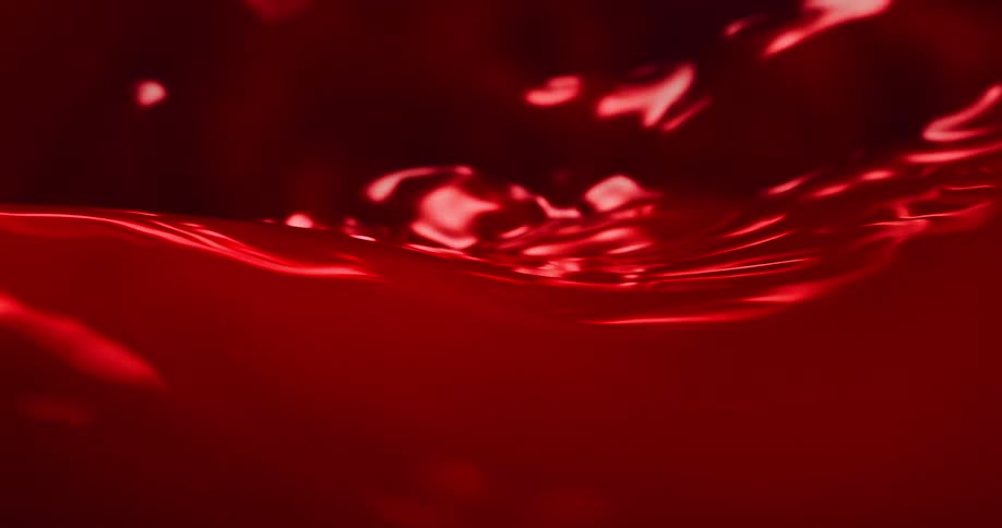 Ripples move across a shiny red liquid surface and splashes as it moves and waves