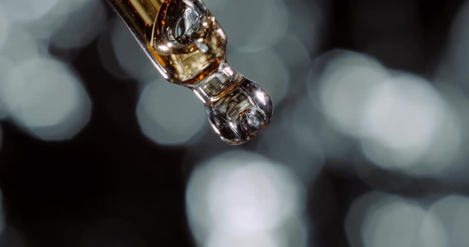 Clear liquid bubbles move inside a small glass container as soft white lights glow in the distance