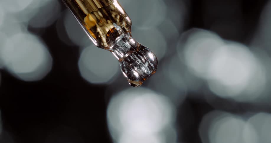 Bubble forms in glass dropper holding amber liquid against a background of white blurry spots