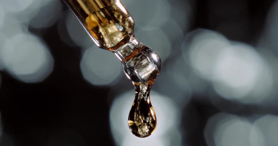 Amber drop falls from dropper leaving small amount held by surface tension