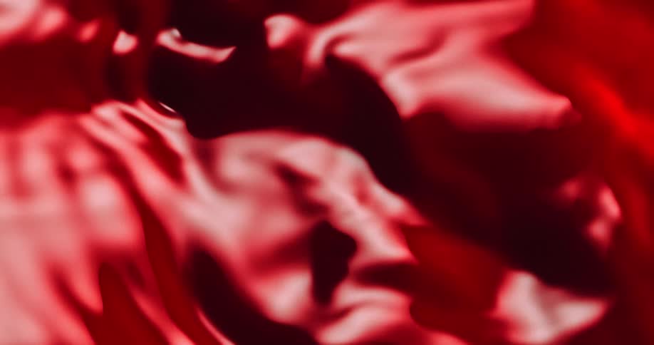 Light shines on an organic red liquid substance as it spreads and moves across the darkness