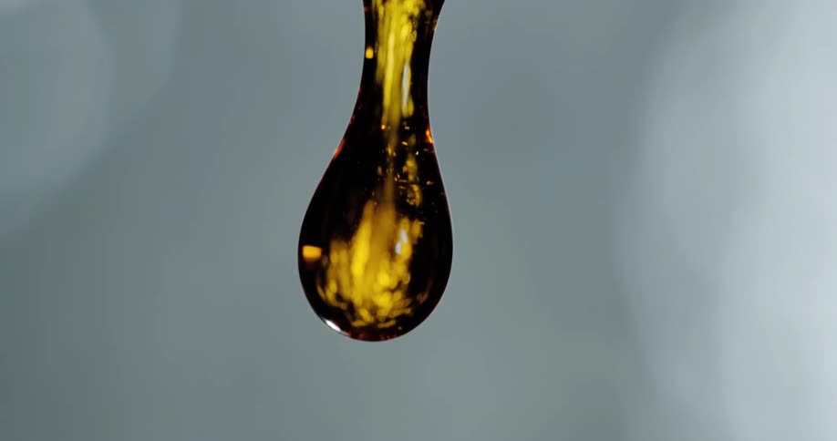 A close up of oil dripping and dropping down with a white background