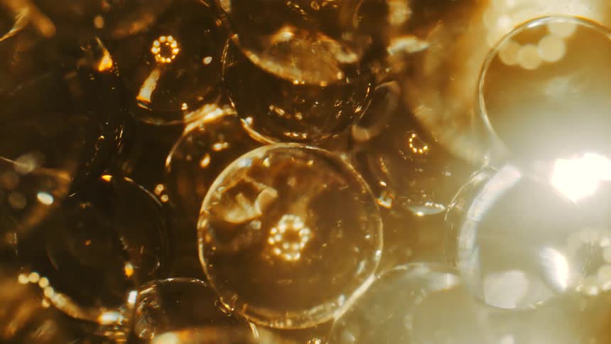 A multitude of transparent gold balls or bubbles are blurry and slowly come into view little by little as the camera backs away