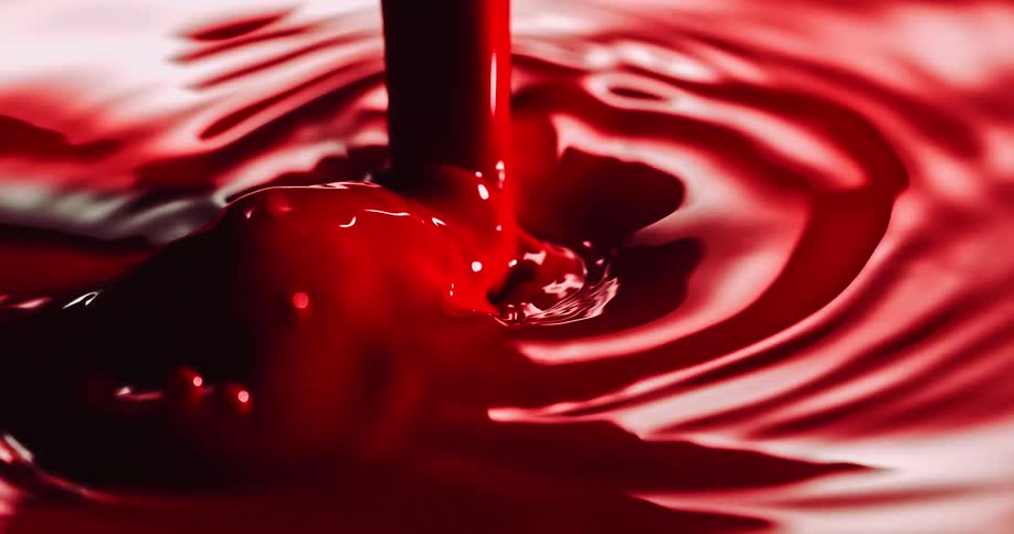 A thick red liquid is pouring into a puddle splashing and rippling as it moves