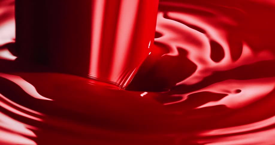 A thick red liquid is pouring into a puddle and rippling as it moves
