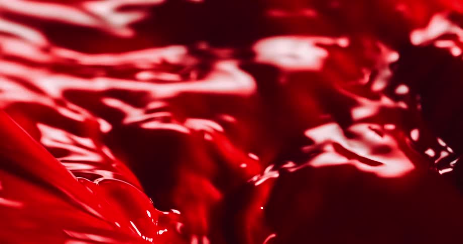 Vivid crimson fluid churns and flows while reflecting light and small drops fall