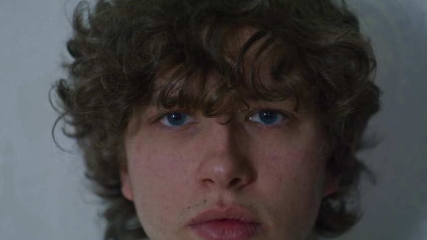 A closeup shot of a young man with a sad and rough expression on his face he has curly hair on his head that adds to his unique look