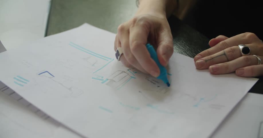A woman uses a highlighter to outline sketches on paper