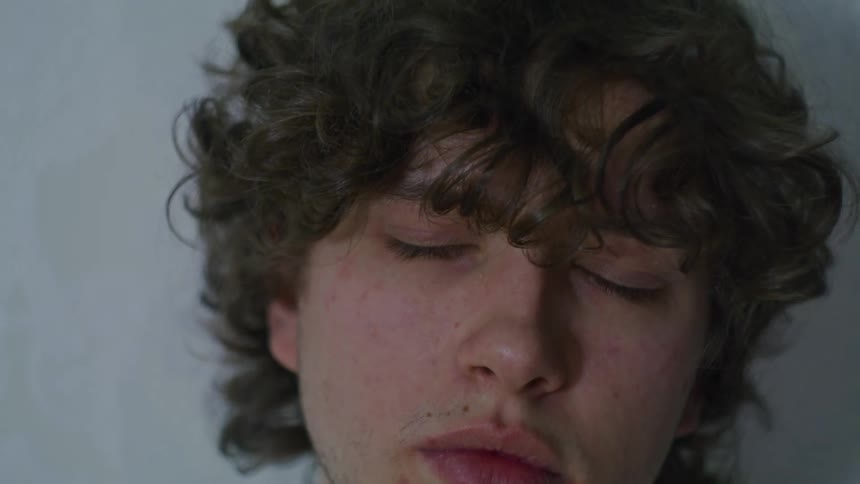 Man with curly hair and blue eyes opens his eyes