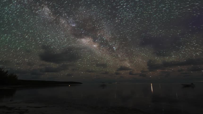 A time lapse of water at night and a full starry sky with reflections on the water