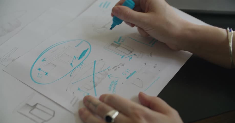 A woman uses a blue highlighter to markup a printed schematic