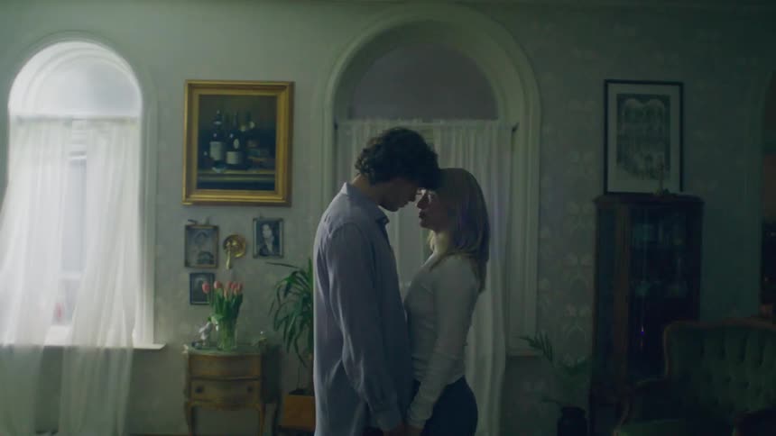 A couple stand with their foreheads touching in their living room