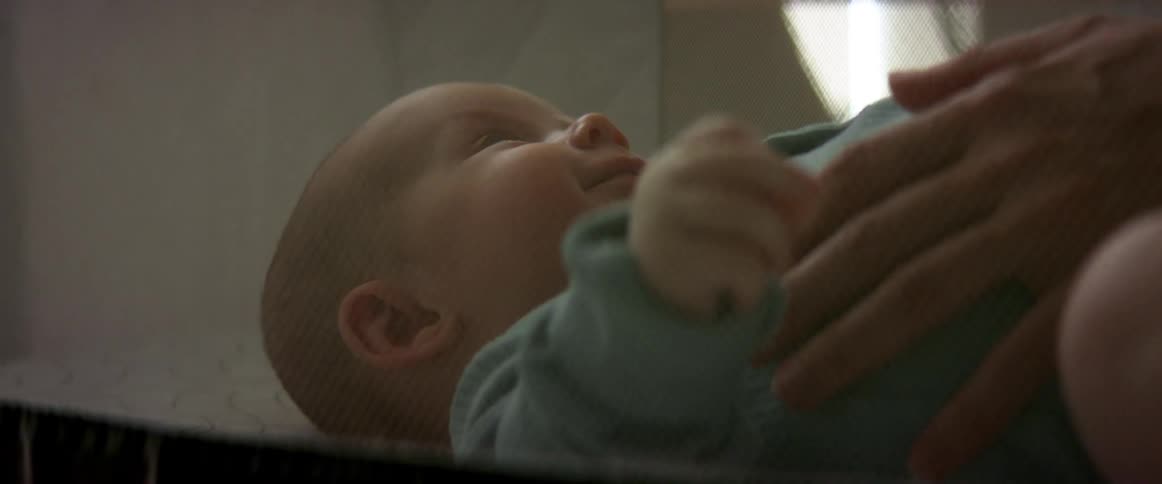 A baby is lying down smiling and moving their head and arms and their mother has her hand on their side