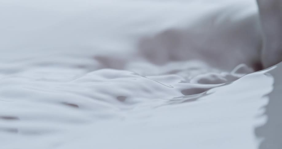 White liquid pours into a puddle and ripples as it moves across the surface