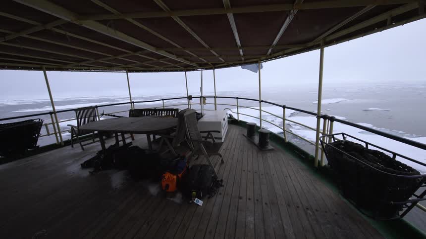 A table and some seats sit on a boat sailing in icy water