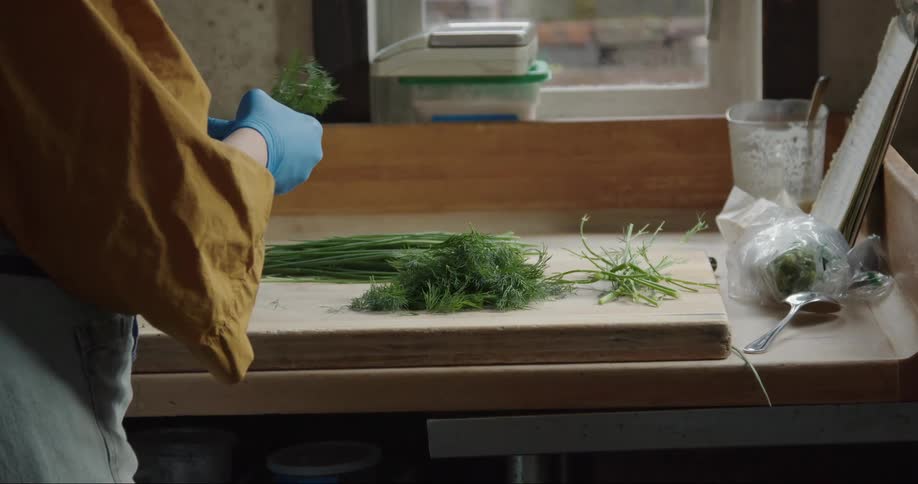 A woman wearing blue gloves is putting herbs in a pile on the cutting board