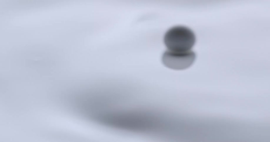 Light shines on pouring white liquid as a white orb bounces and moves across the surface and then falls in as the liquid ripples and moves