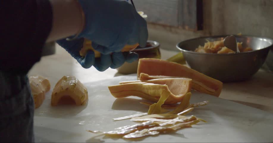 Woman with blue gloves uses peeler to peel yellow squash in the kitchen