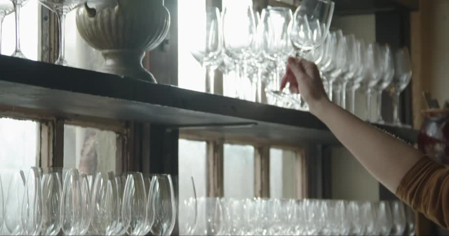 A bartender puts a wine glass on the top shelf with other wine glasses